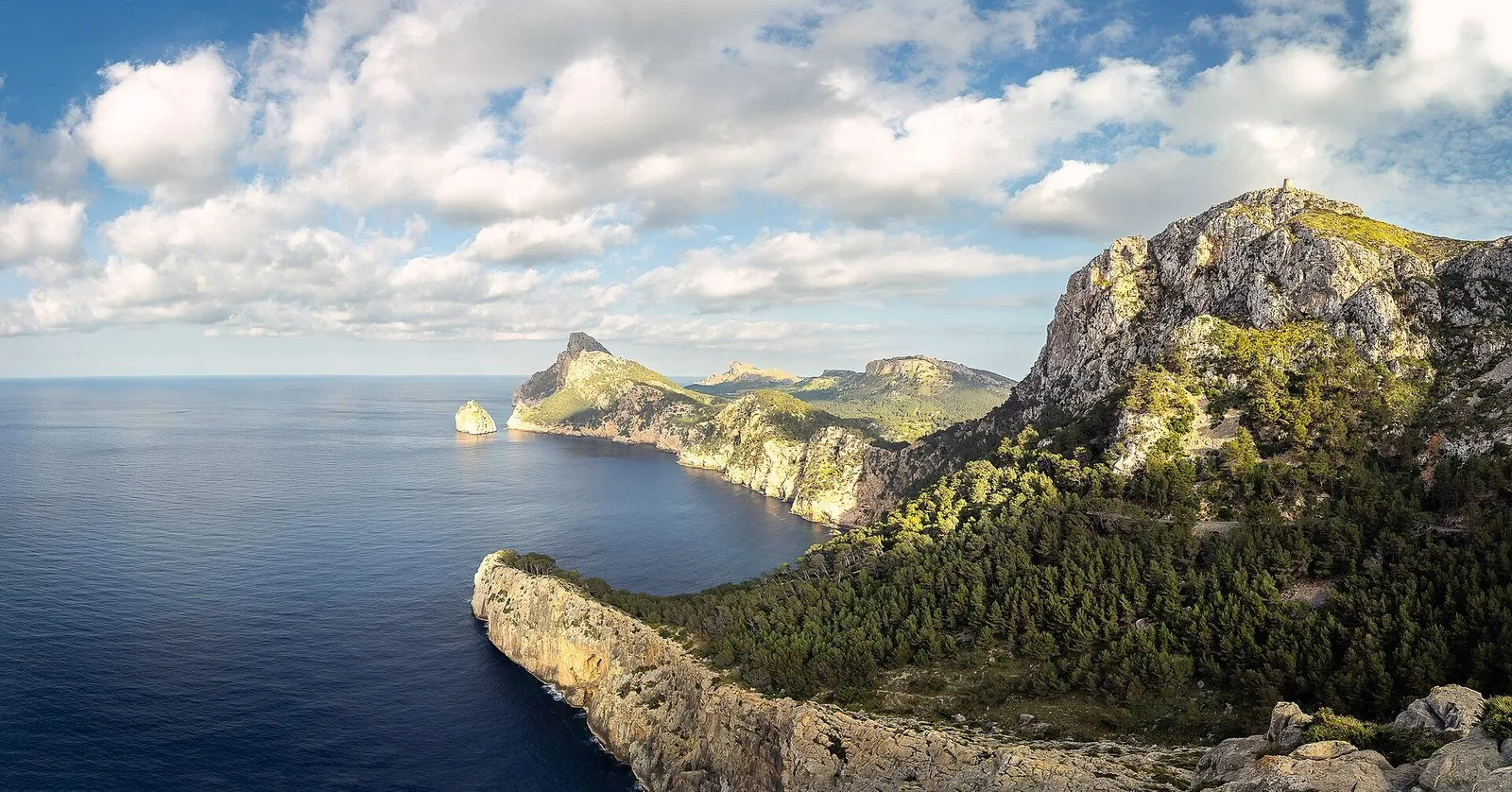 Headland with cliffs, woodland and blue sea under a cloudy sky