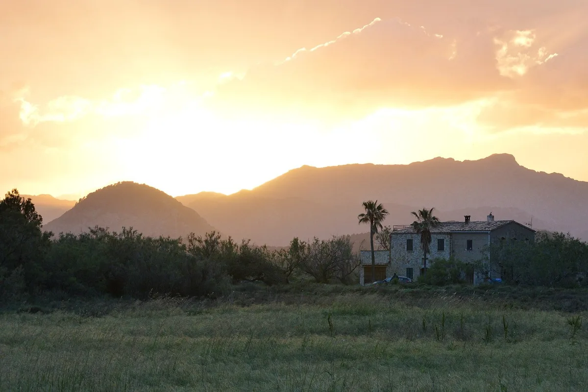 Atardecer sobre una montaña y una casa entre campos