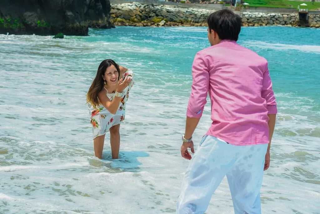 Couple standing in shallow water at the shore, she taking a photo