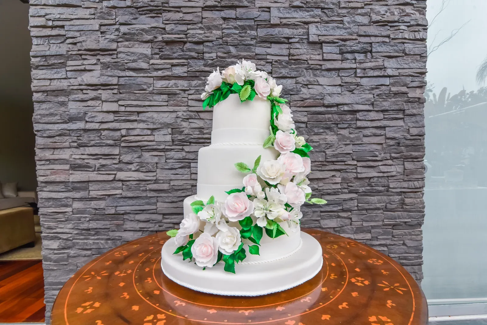 Three-tier wedding cake with white roses on a stone table