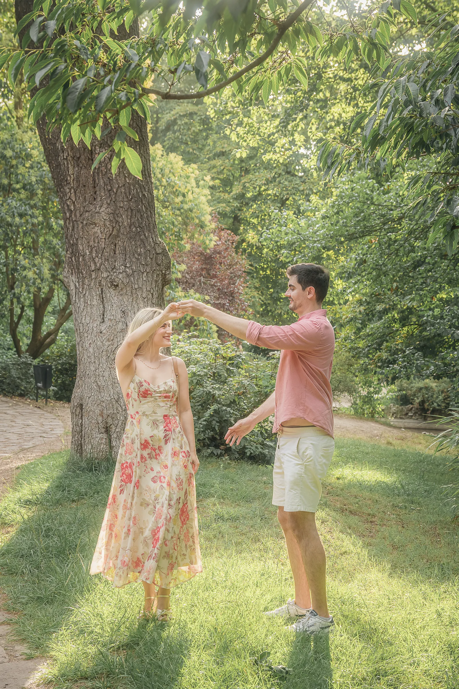 A couple among trees in a park, she twirling in a flowered dress