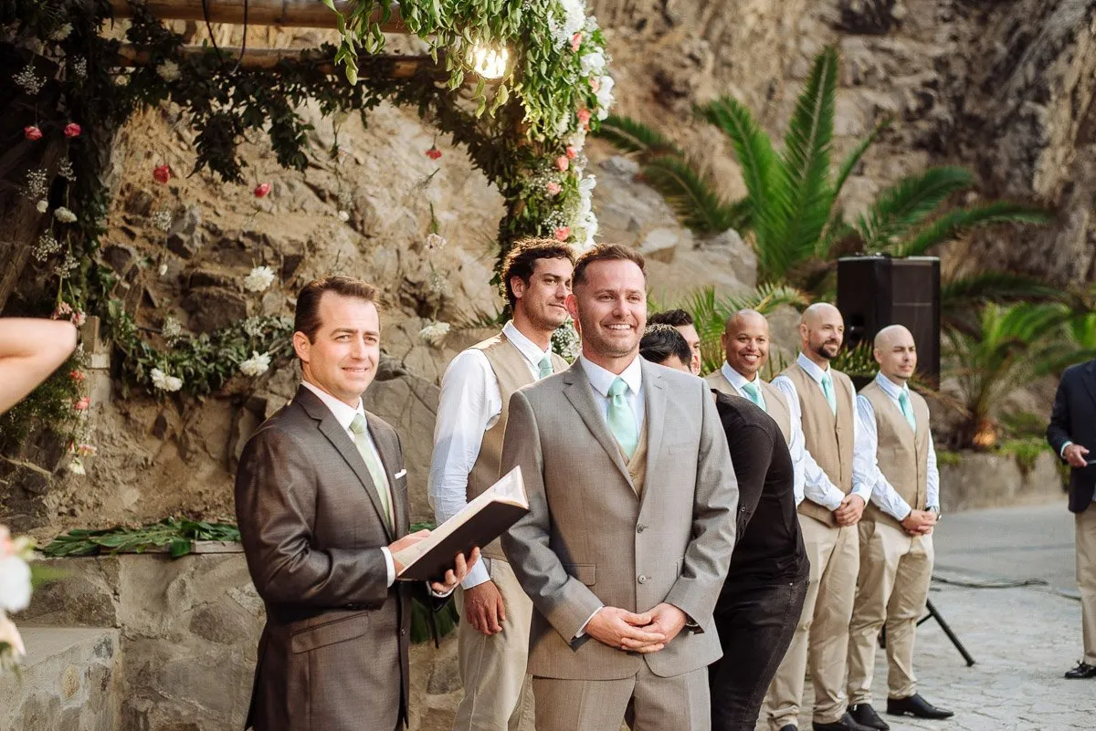 The officiant reads from a book before the groom, in a ceremony beside rocky cliffs