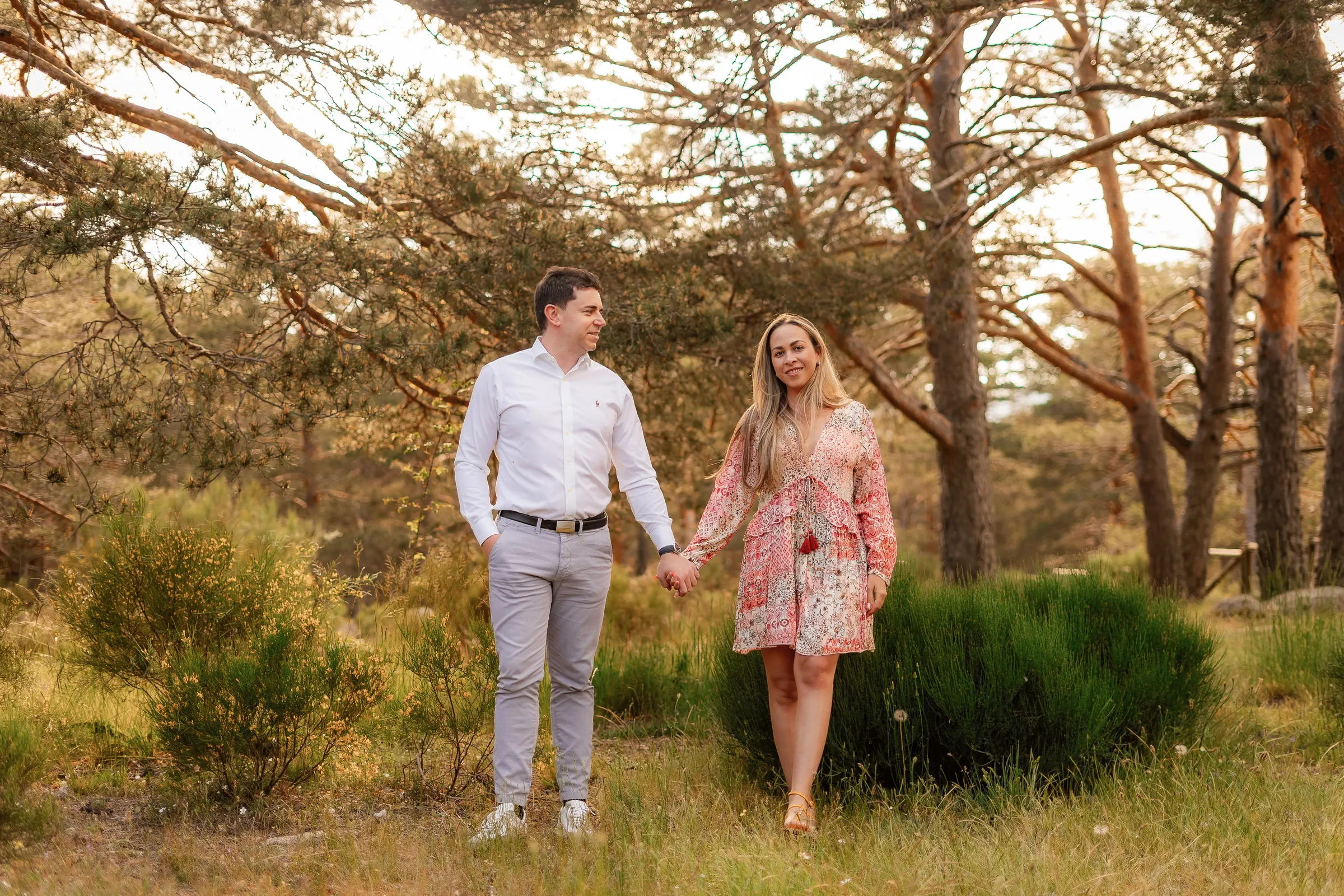 Pareja caminando de la mano entre pinos y matorral