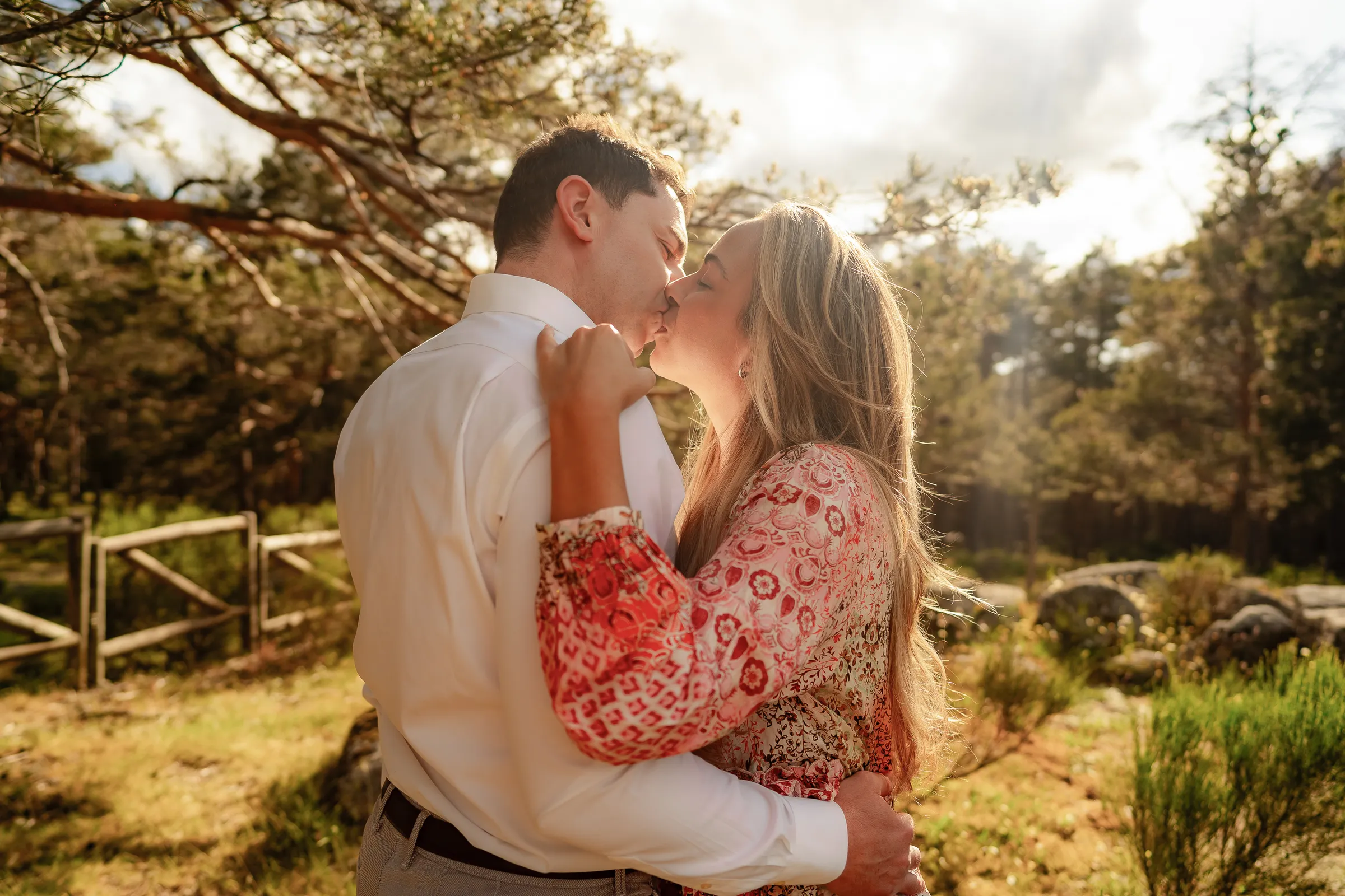 Couple kissing beside a wooden fence in a pine grove