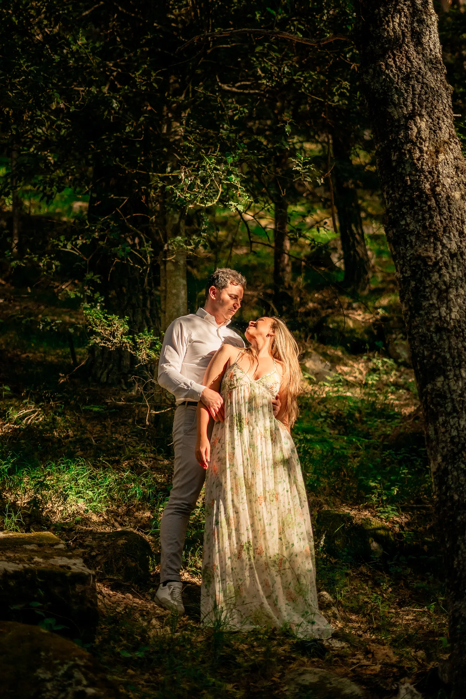 Pareja con vestido largo entre árboles en un bosque