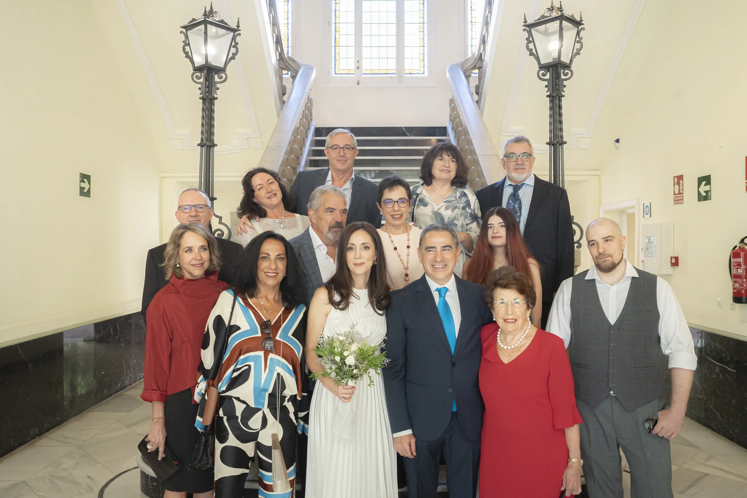 A large family group poses on a staircase; in the centre, a woman in white holding a bouquet