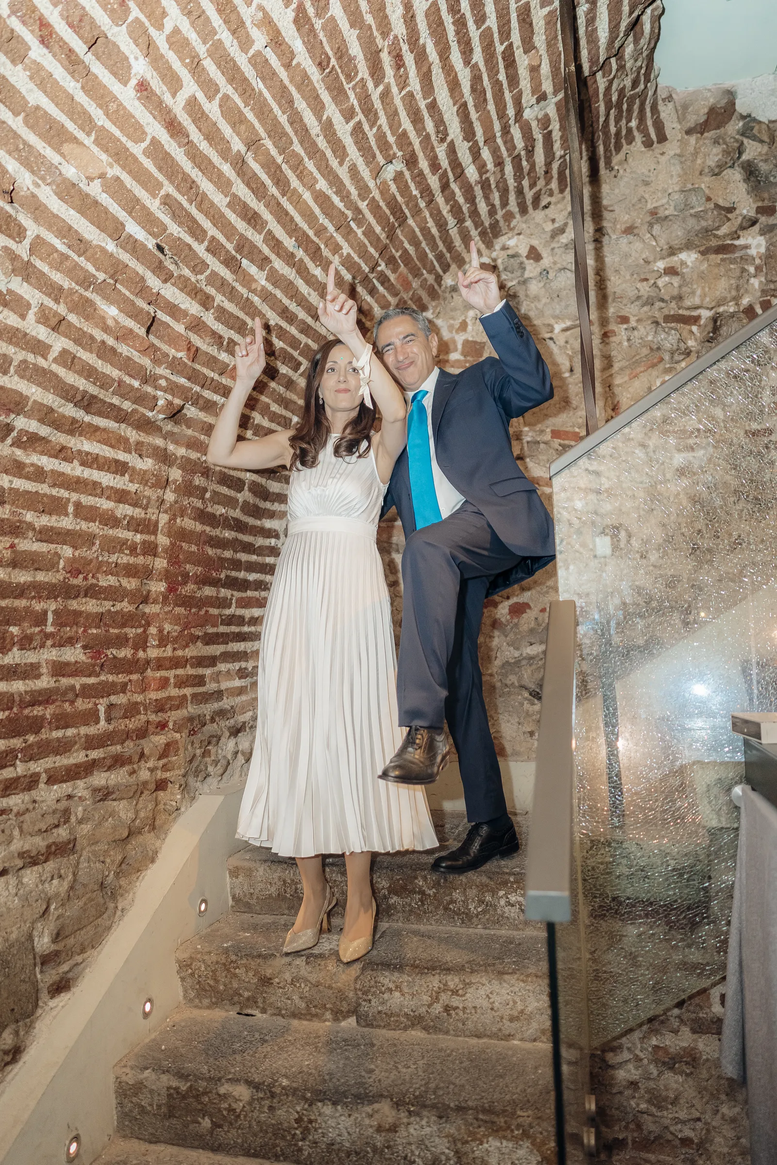 Bride climbing a staircase beside a brick wall