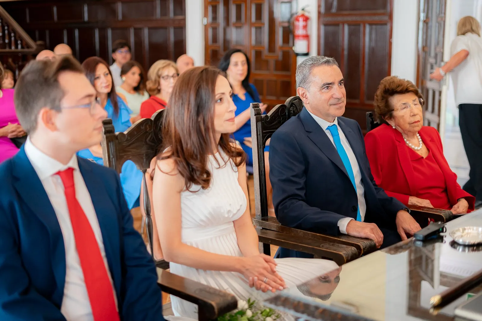 The couple, seated among their relatives in a room with wooden walls, during the ceremony