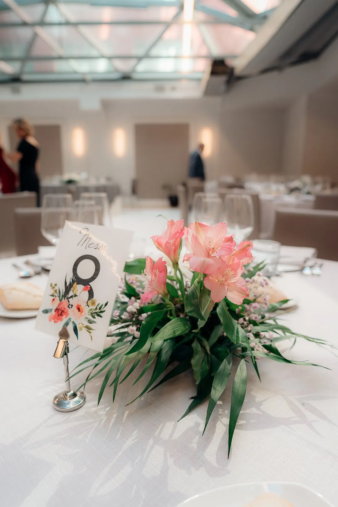 Mesa redonda con número de mesa y un centro de flores rosas en un salón de banquetes