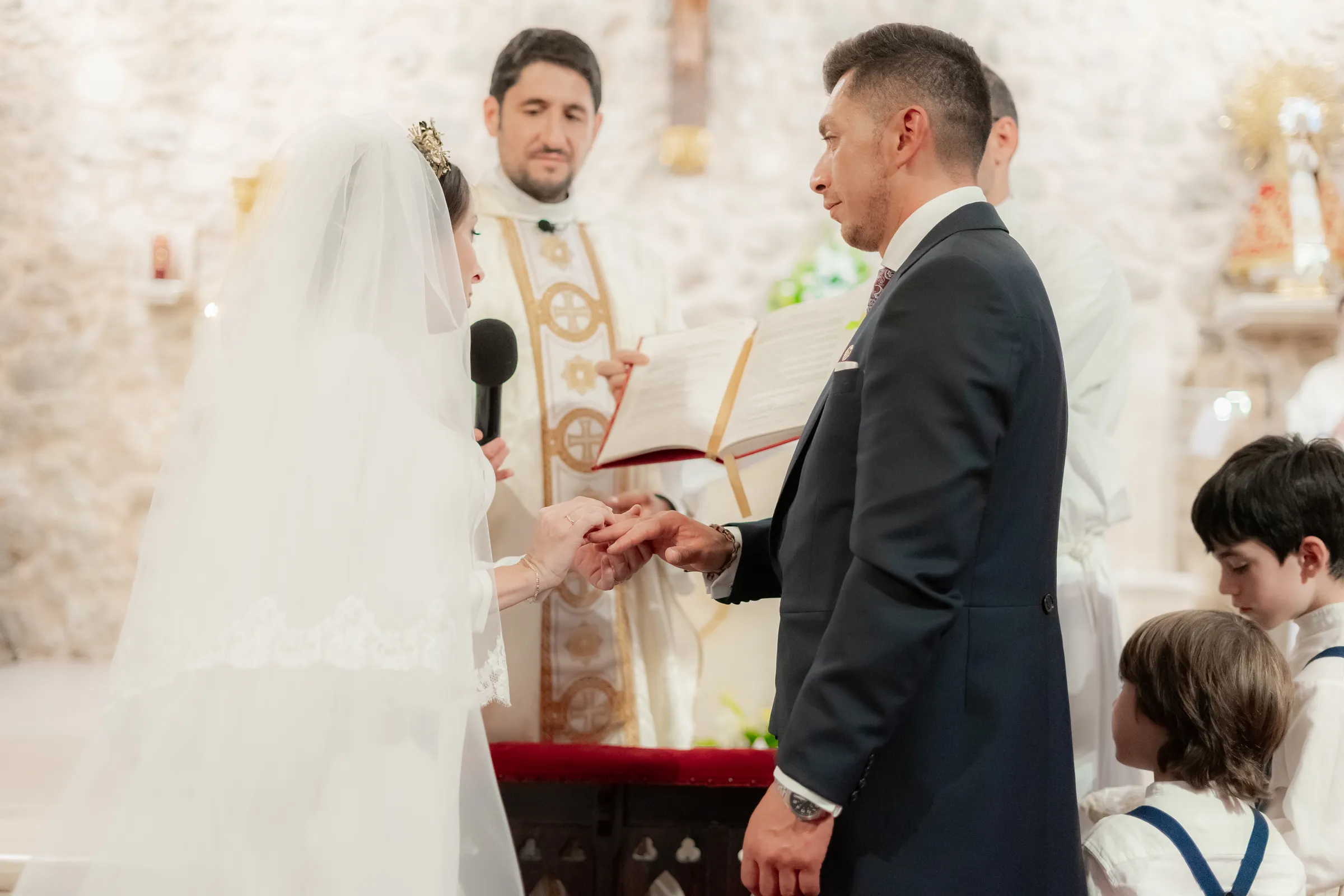 The groom places the ring on the bride before the priest during a religious ceremony