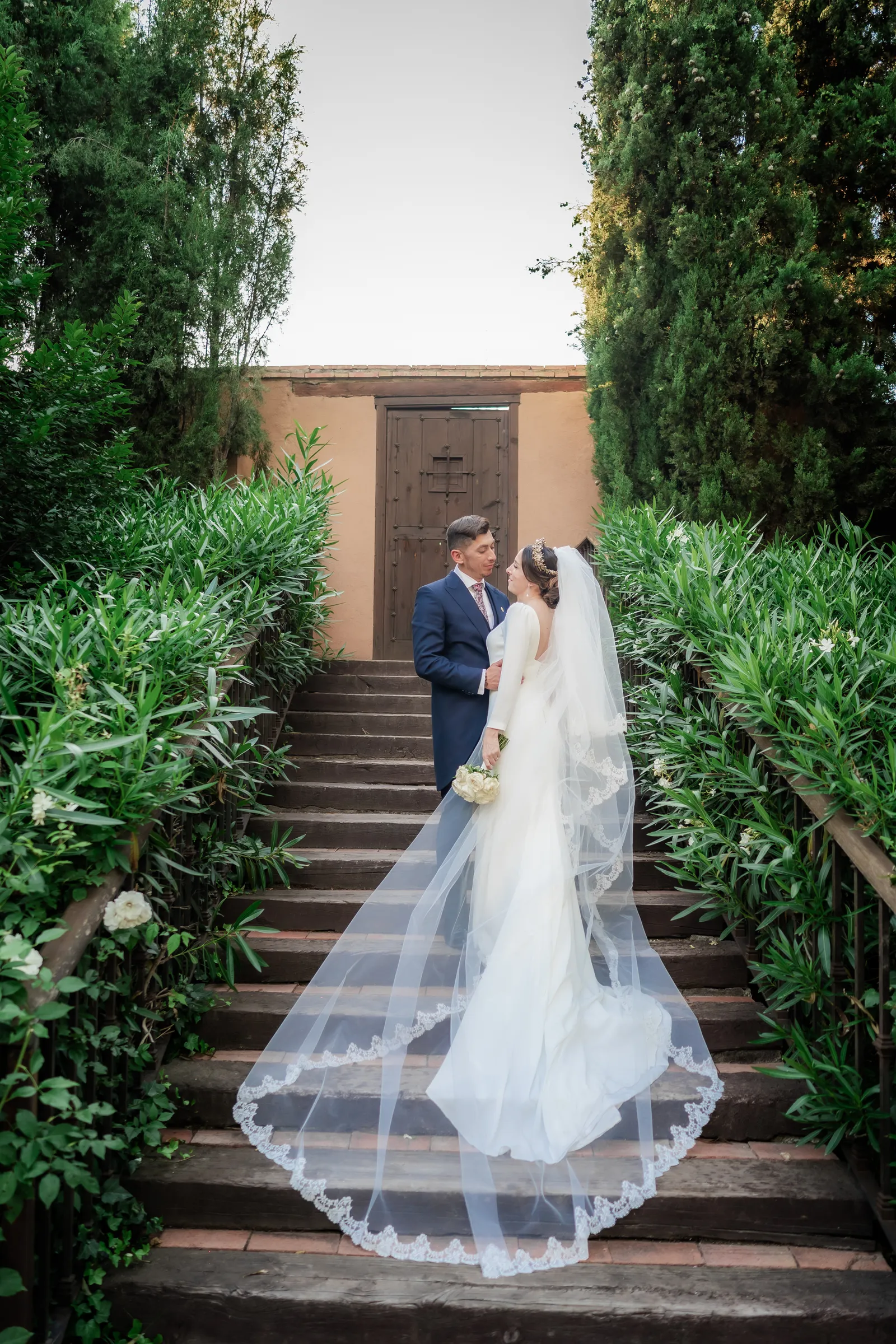 Bride with a long veil on a stone staircase between hedges
