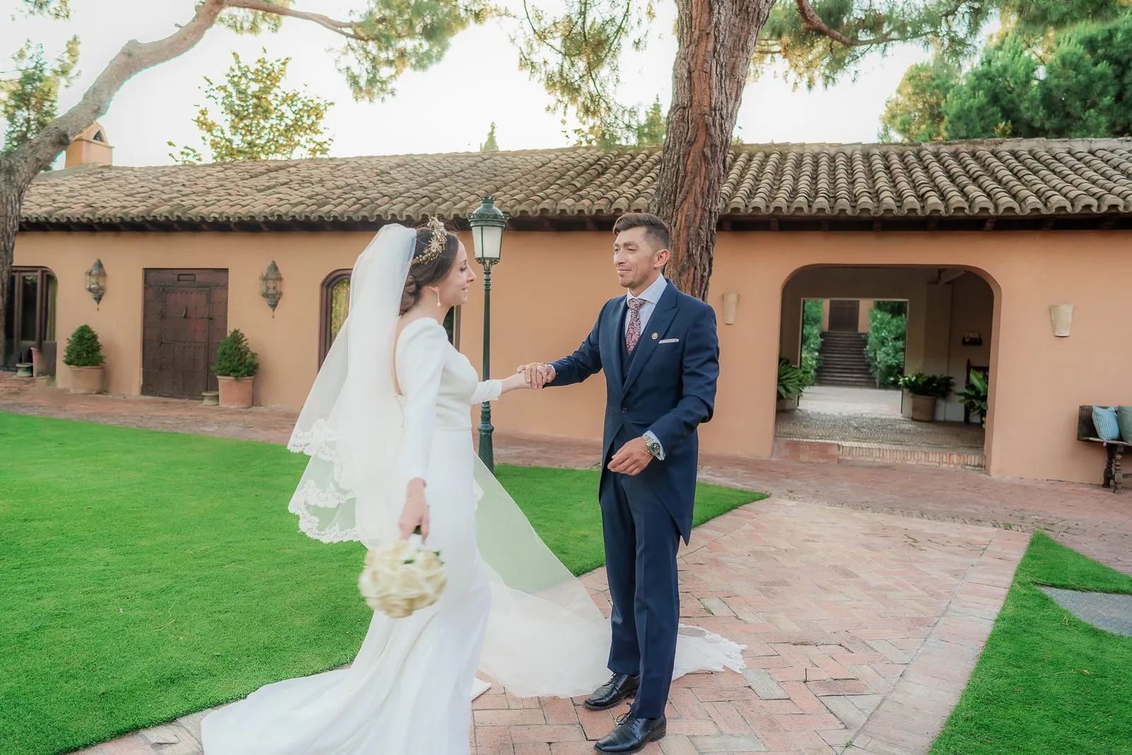 Novia y novio sobre el césped, ante una casa de ladrillo y teja