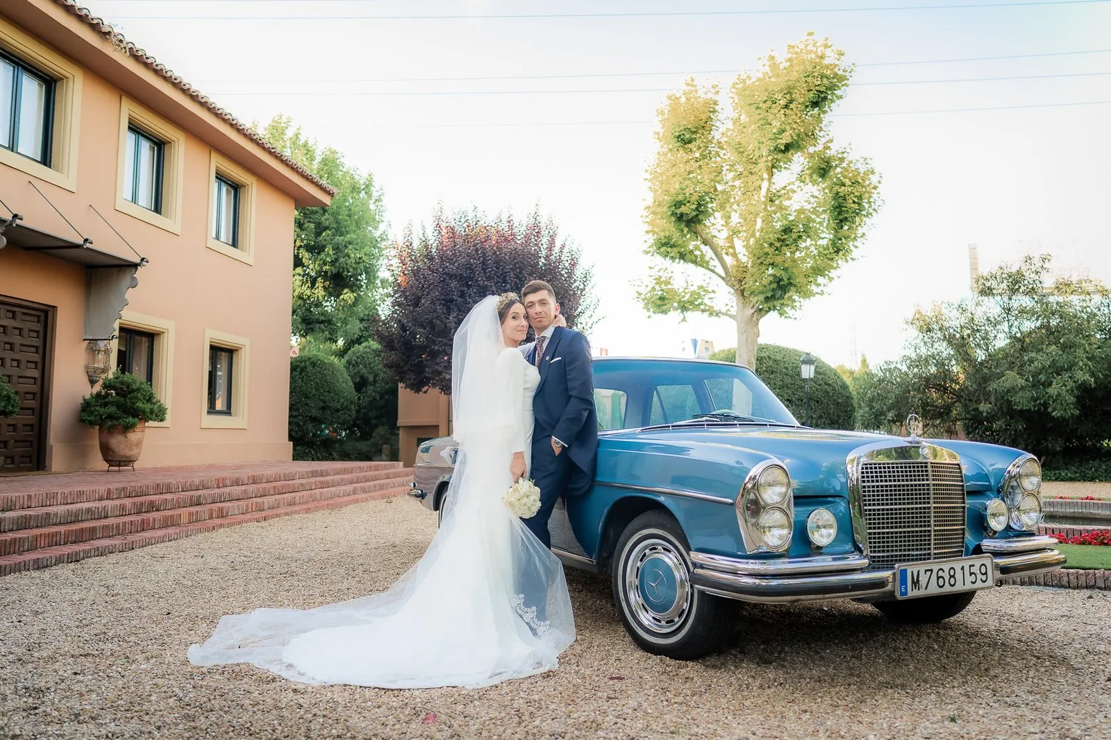 Bride beside a classic blue car in front of a house