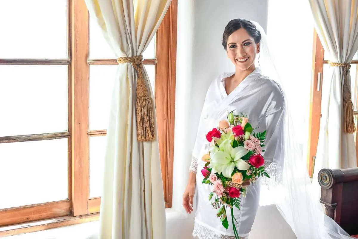 Bride with a bouquet beside a curtained window