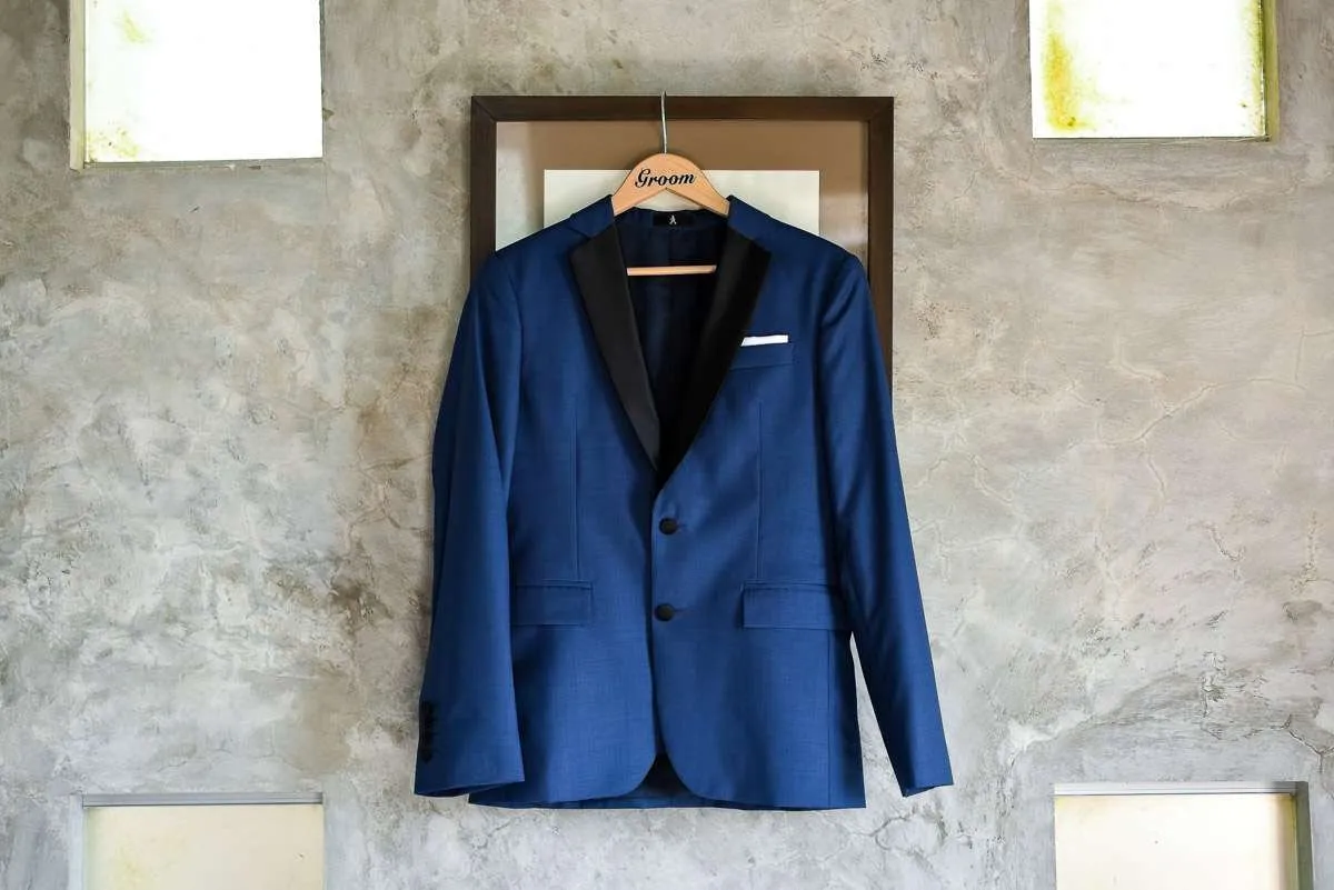 A navy jacket with black lapels hanging from a hanger on a polished concrete wall