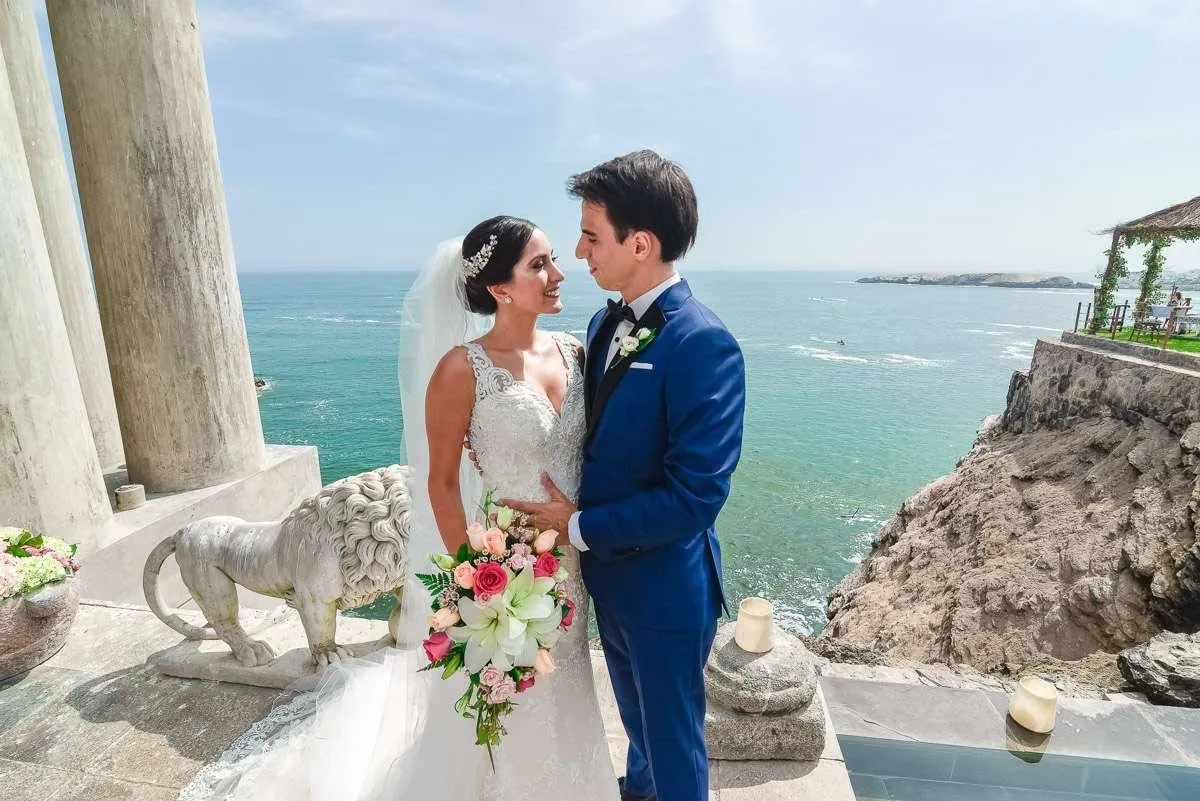 Newlywed couple embracing on a cliff edge, with the sea behind them
