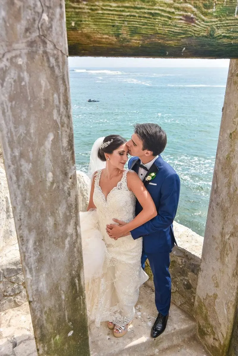 A couple embracing between two stone pillars, the sea behind them