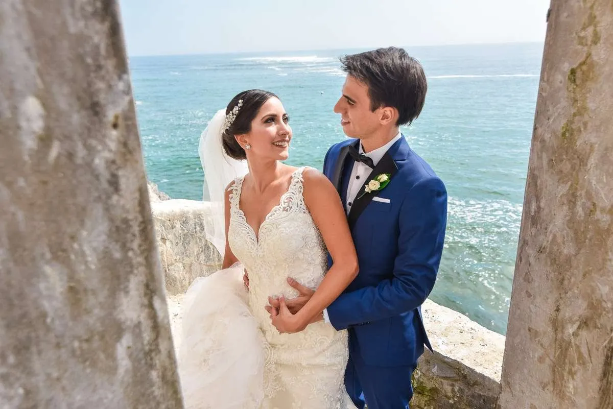 Couple embracing between two stone columns, with the blue sea behind