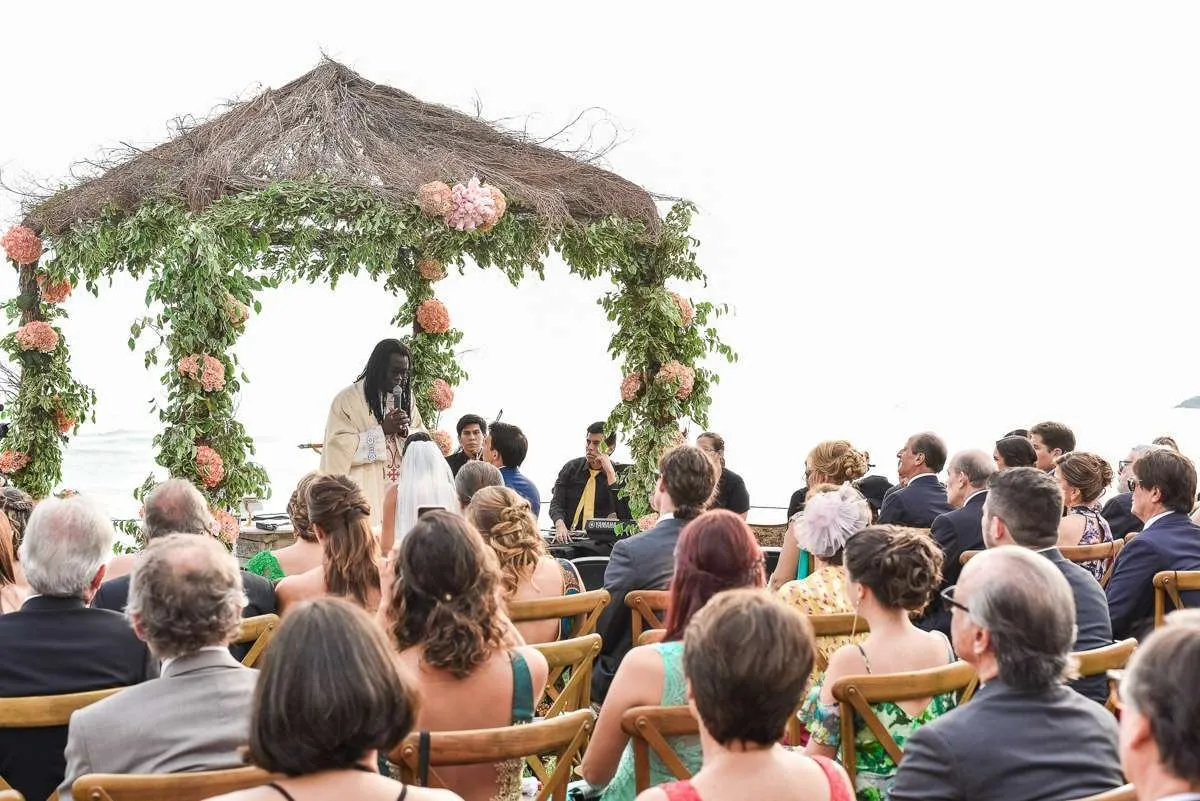 A ceremony under a flower-covered pergola, with guests seated facing the couple