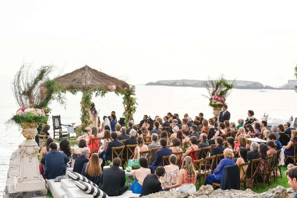 Open-air ceremony facing the sea, with guests seated under a clear sky