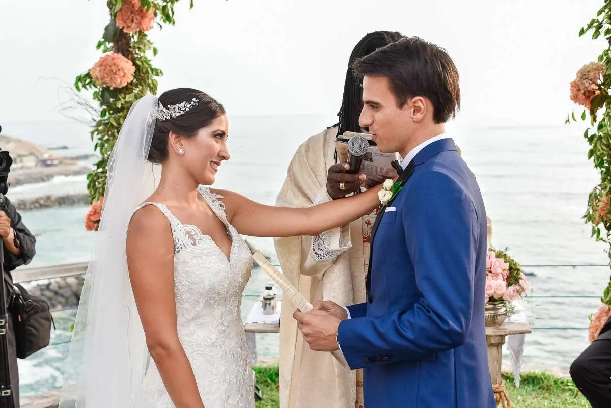 The bride hands the groom a text during the ceremony, with the sea behind them