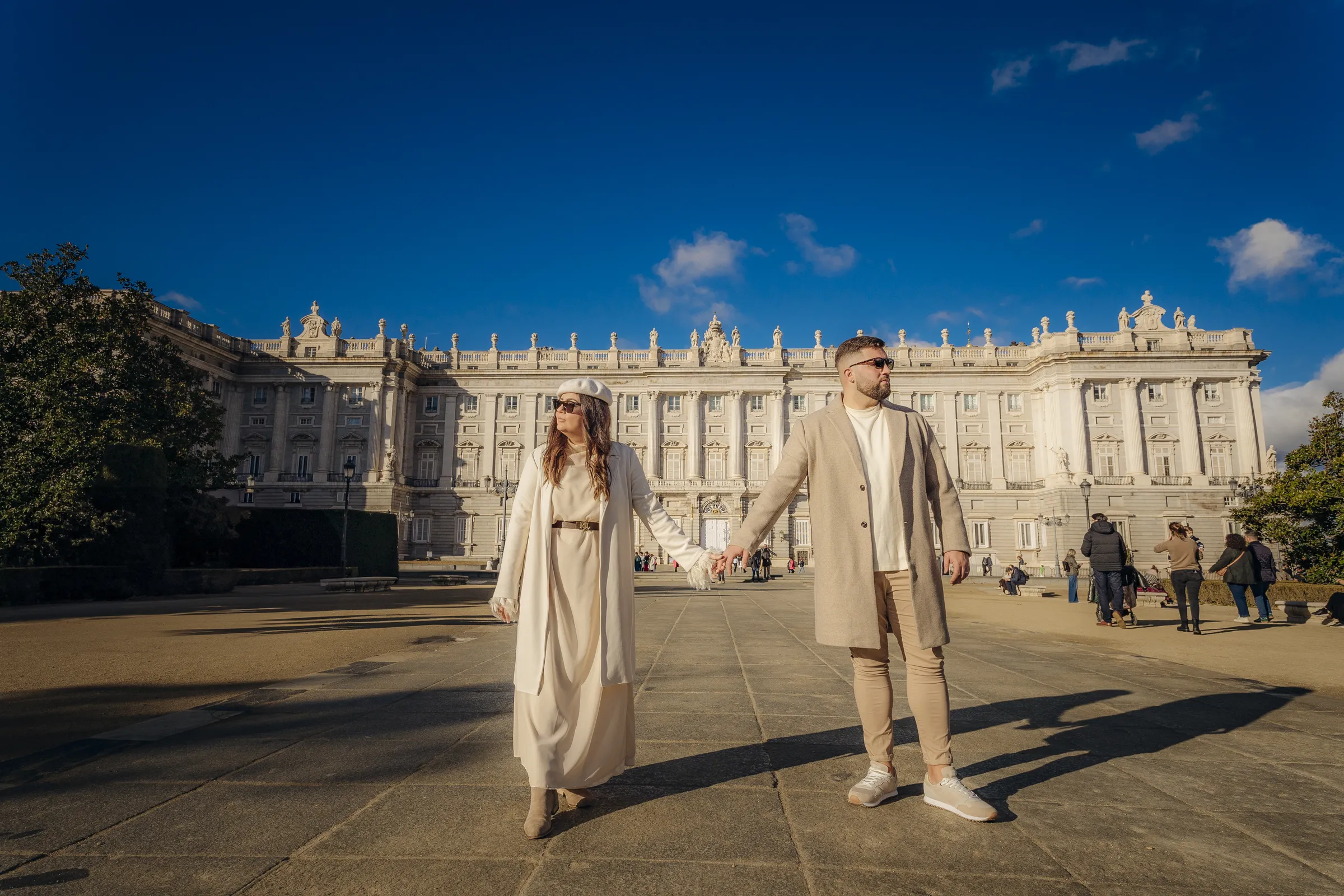 A couple embracing in front of a large stone building, in a sunny square