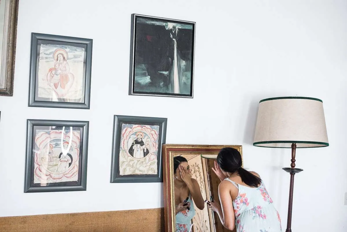 A guest at a mirror in a white room, lit by window light
