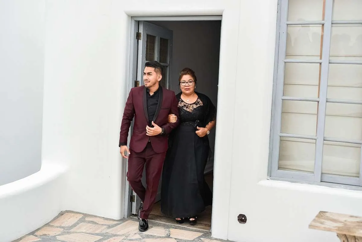 Un hombre de traje granate sale de un portal blanco junto a una mujer de vestido negro