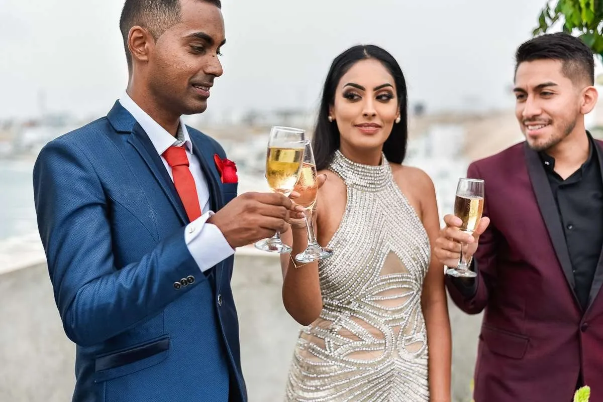Tres invitados brindan con copas en una terraza sobre el mar, con luz suave de tarde