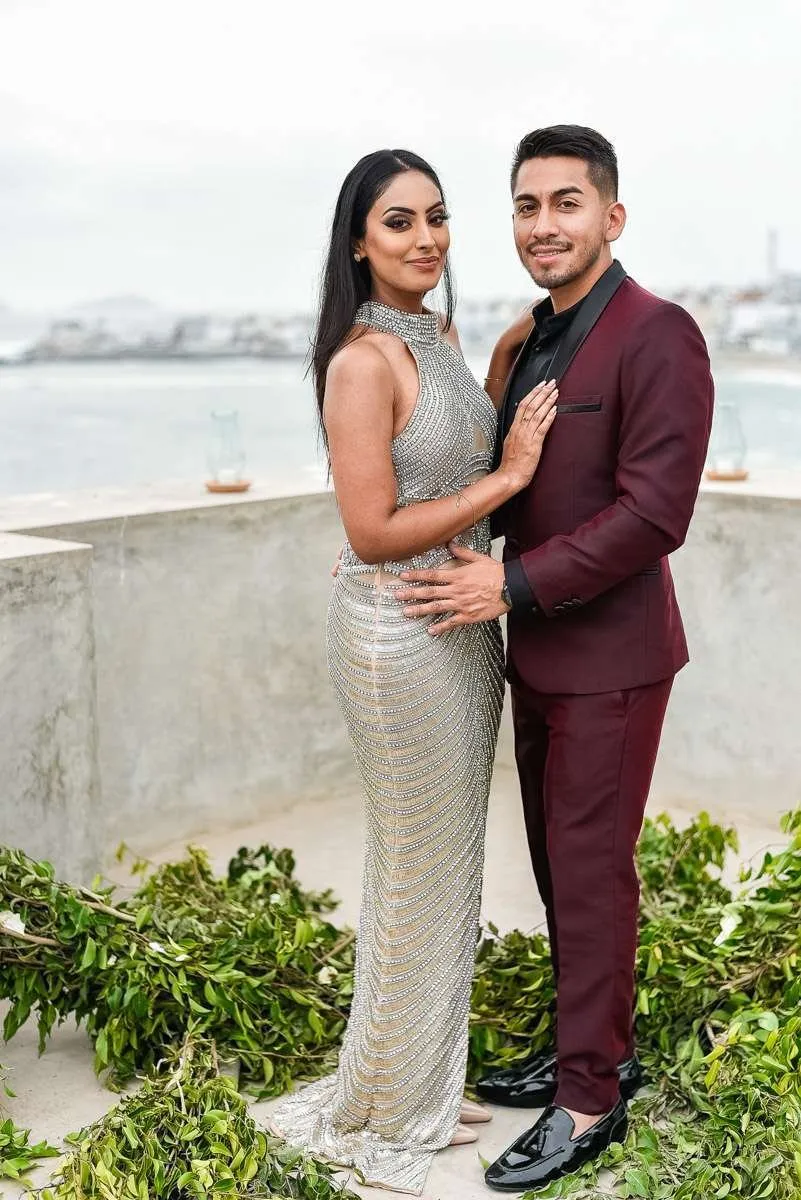 Couple standing on a white terrace, with the sea and coastline behind