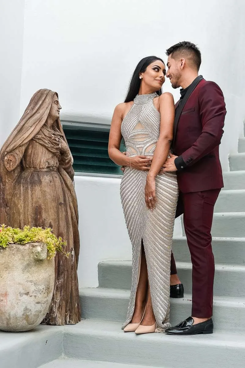 Los novios, abrazados y mirándose, ante una escultura de madera en una escalera blanca