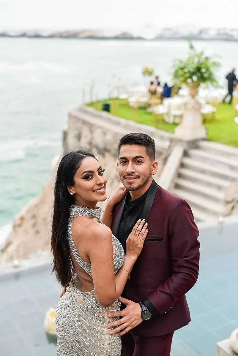 A couple smiling to camera on a terrace above the sea
