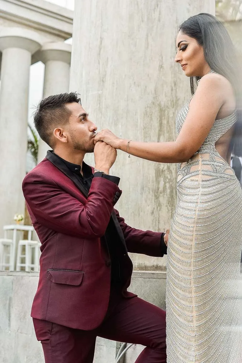 Man kneeling to kiss his partner's hand before stone columns