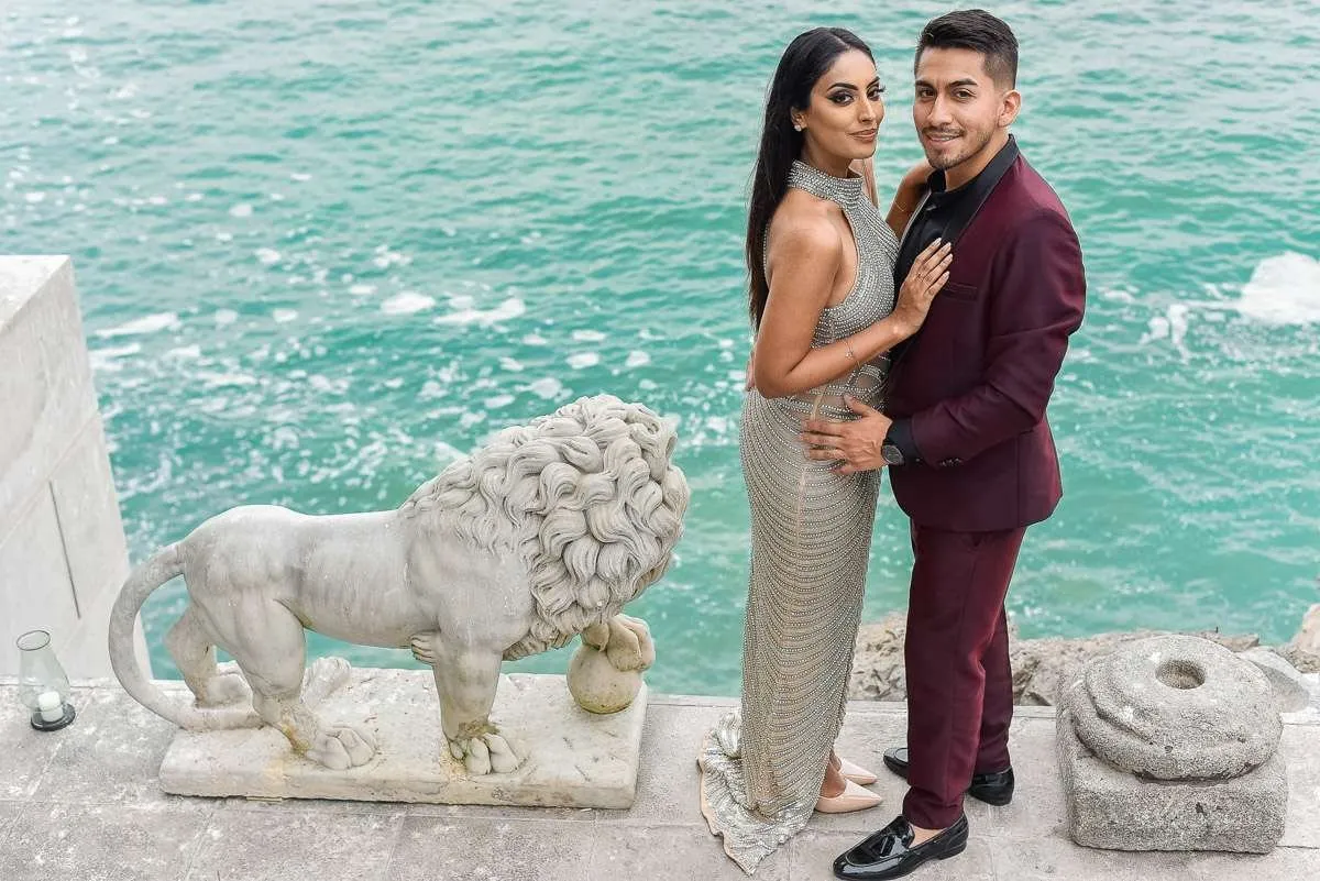 Couple embracing above a turquoise sea, with a stone lion beside them