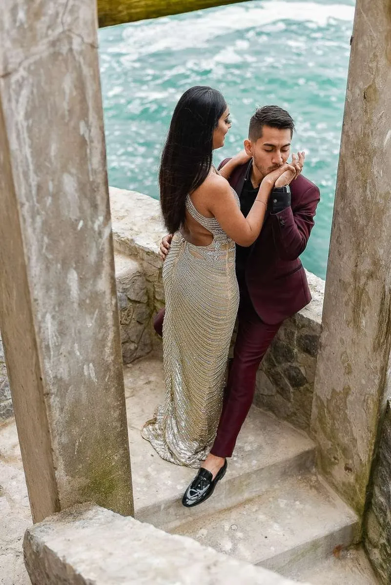 Couple between stone columns, he kissing her hand, with the sea behind