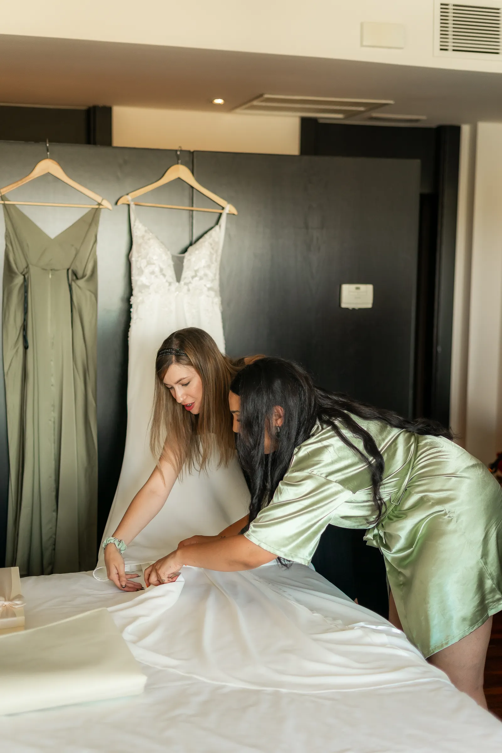Dos amigas preparan un vestido de novia junto a otros dos vestidos colgados en la habitación