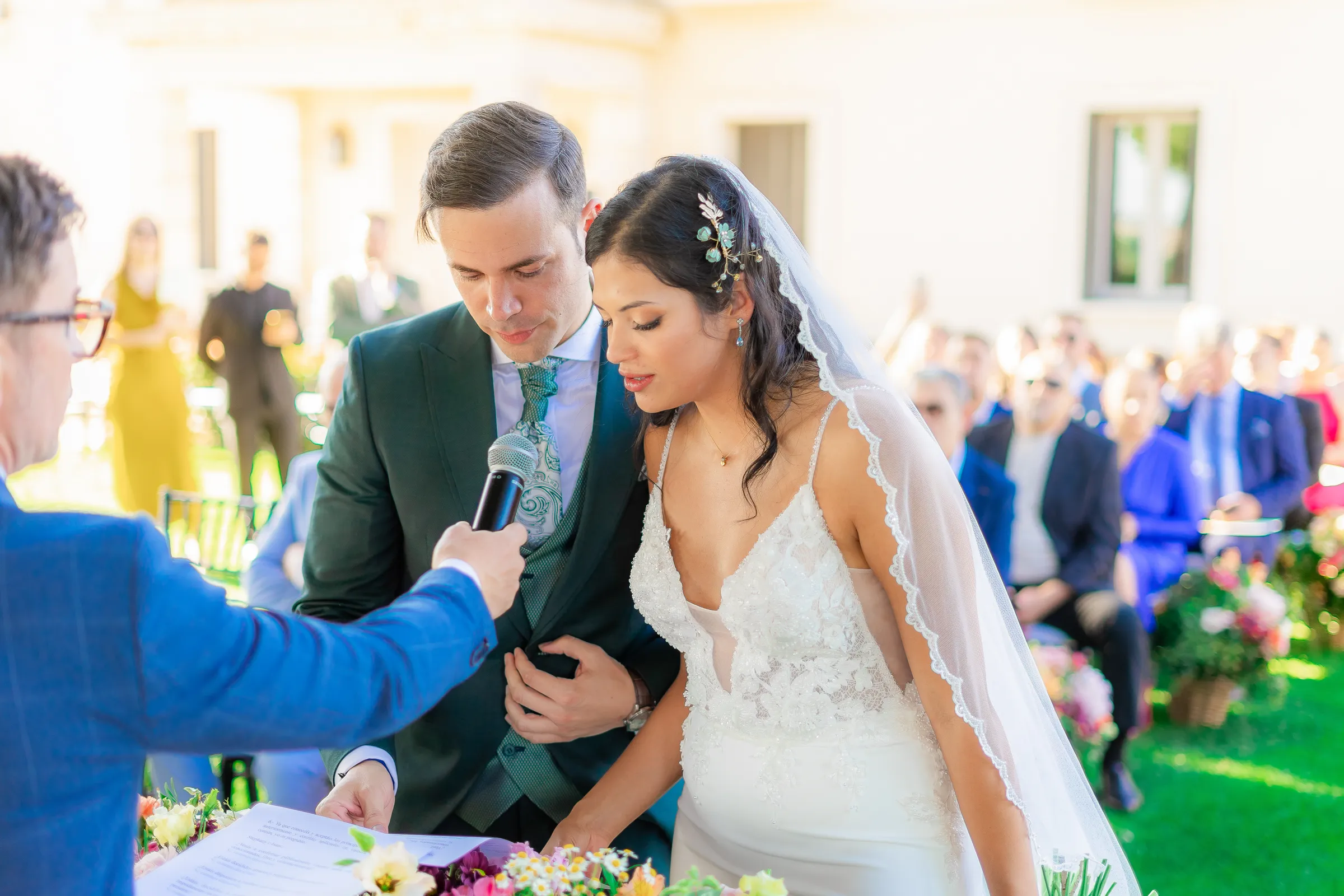 Couple before an officiant with a microphone at an outdoor ceremony