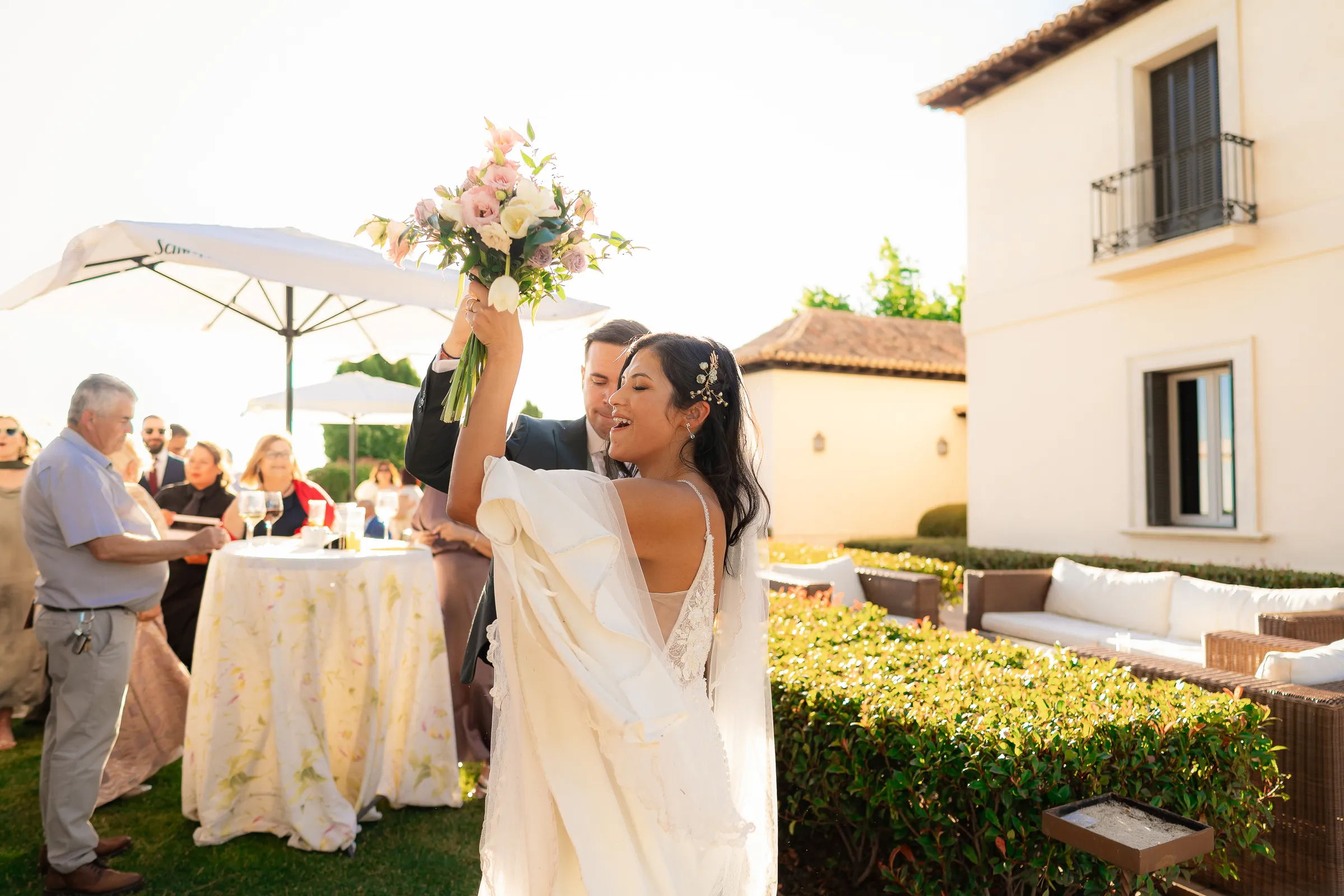 Novia con su ramo junto a una mesa y una sombrilla en un jardín