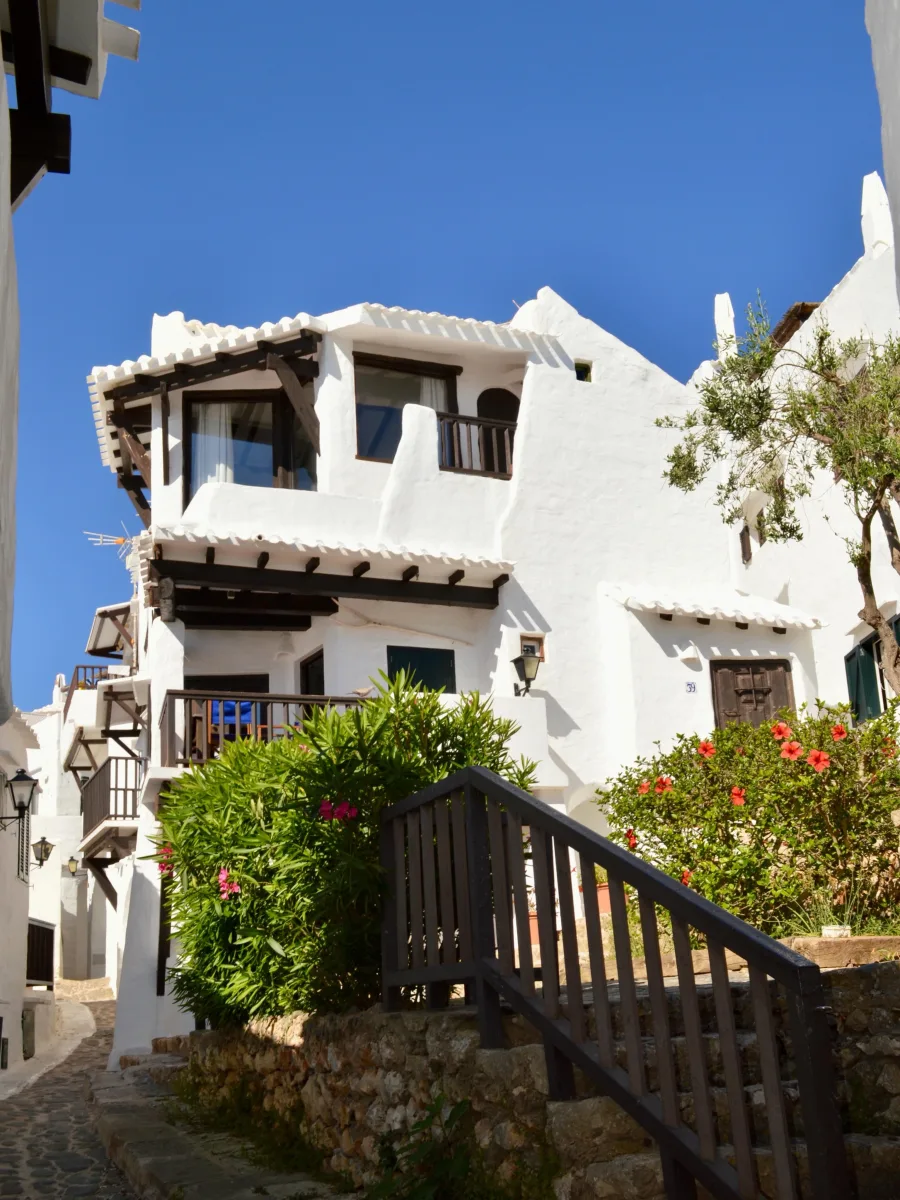 A whitewashed house with terraces, a wooden staircase and red flowers among the greenery