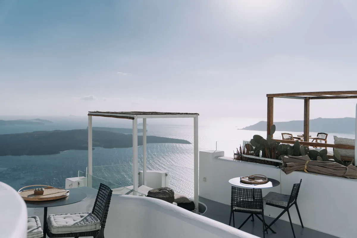 Terraza blanca de un hotel, con mesa, sillas y una pérgola frente al mar y la costa