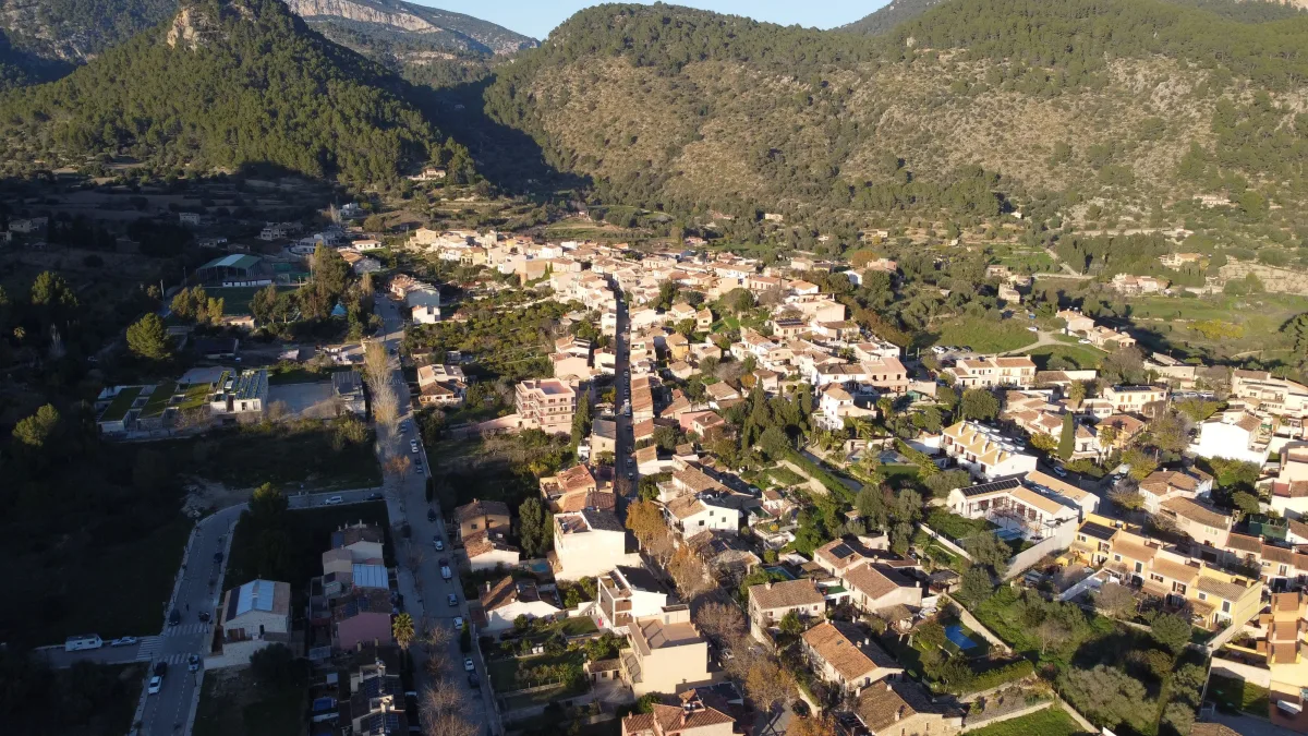 Aerial view of a village at the foot of a mountain range, with streets, rooftops and fields around it