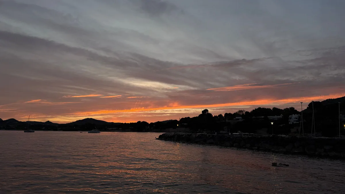 Sunset over a calm sea, with the coastline in silhouette under an orange and grey sky