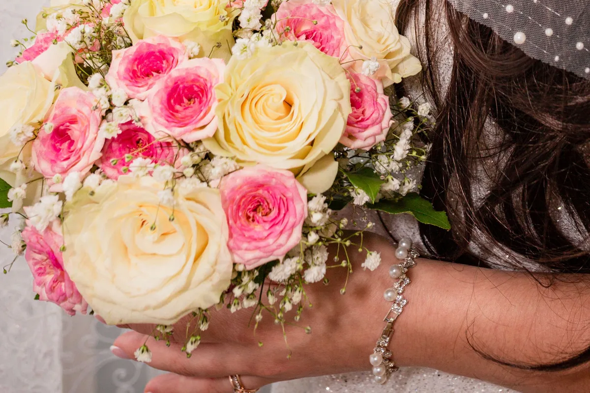 Un ramo de rosas rosas y crema con paniculata en las manos de una novia con velo