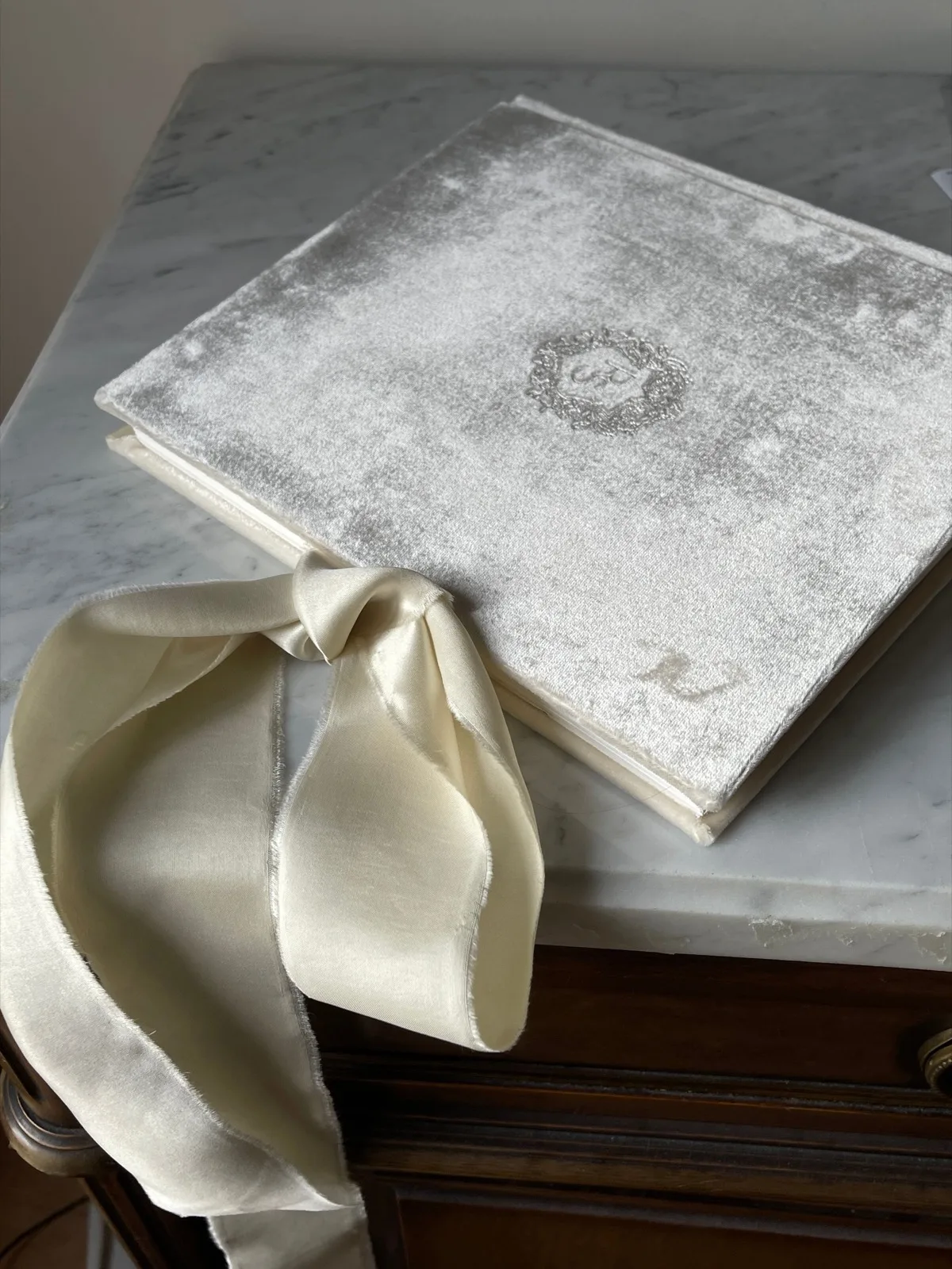Pale grey velvet wedding album with an ivory silk ribbon, on a marble table