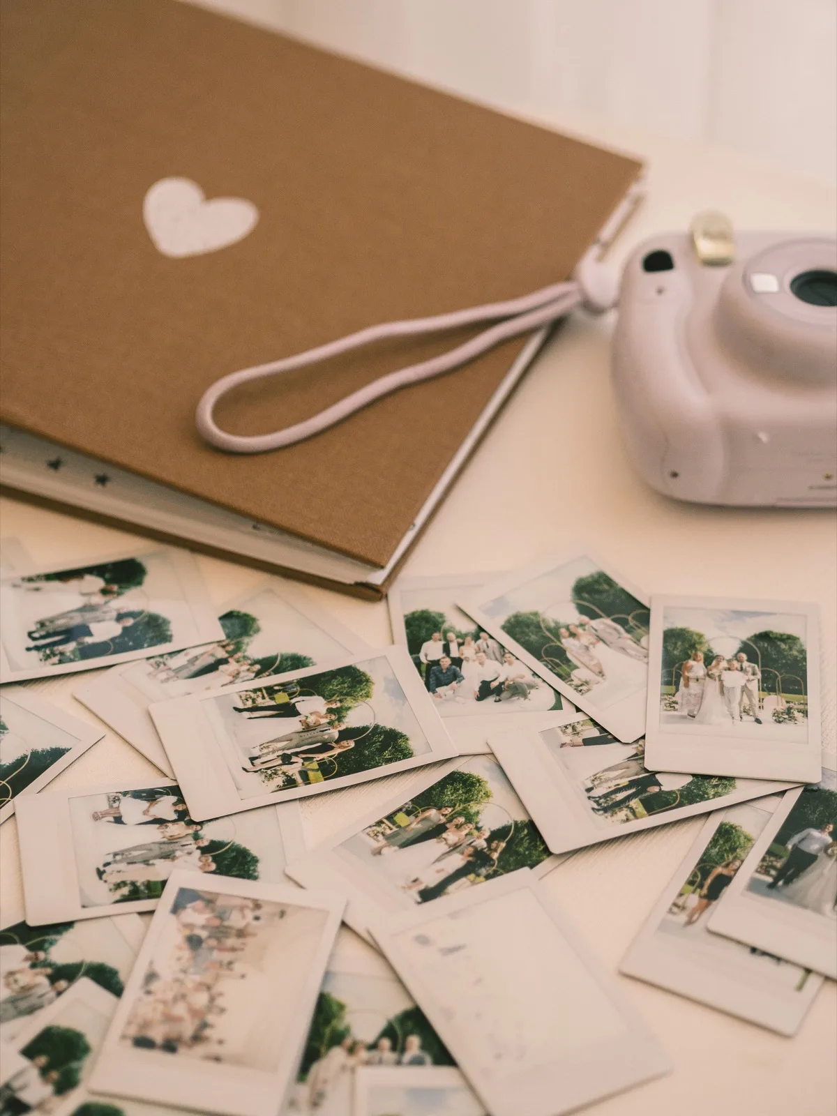 A linen-covered album and instant prints scattered on a white table beside an instant camera