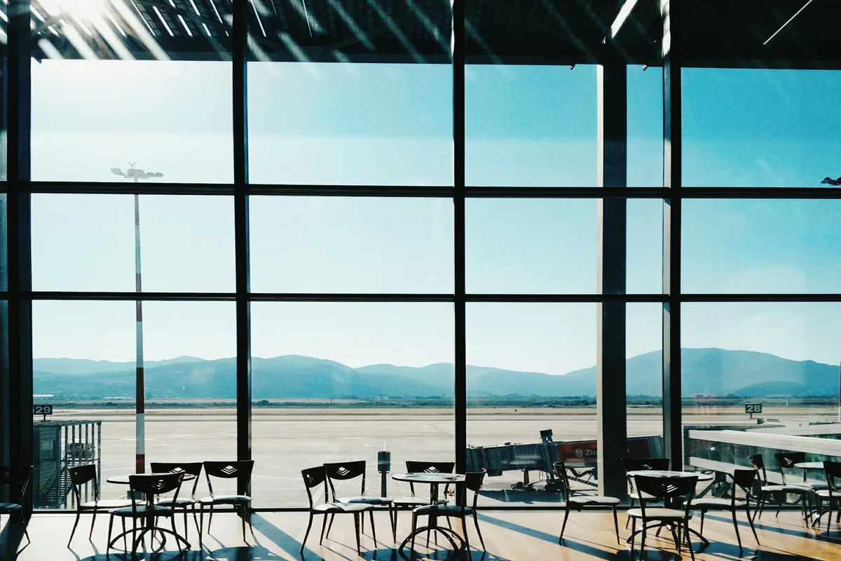 Cristaleras de una terminal de aeropuerto con vistas a la pista y a las montañas, con mesas y sillas vacías