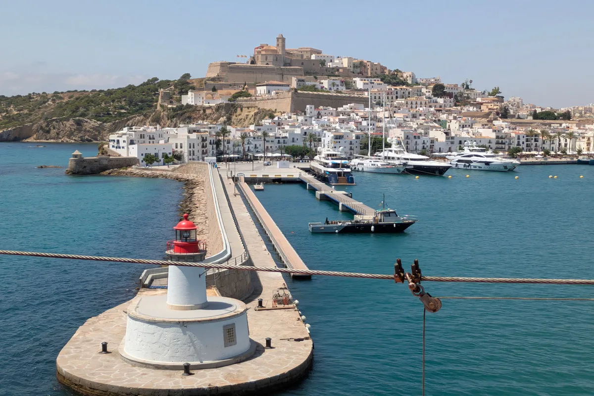 View of Ibiza harbour from the sea, with the red lighthouse on the breakwater and the walled old town on the hill