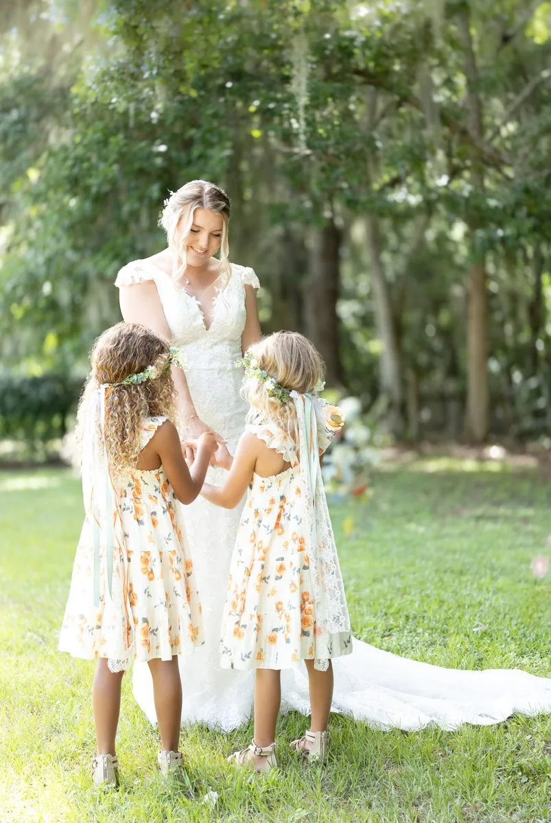 The bride standing in a garden beside two girls in flowered dresses, seen from behind