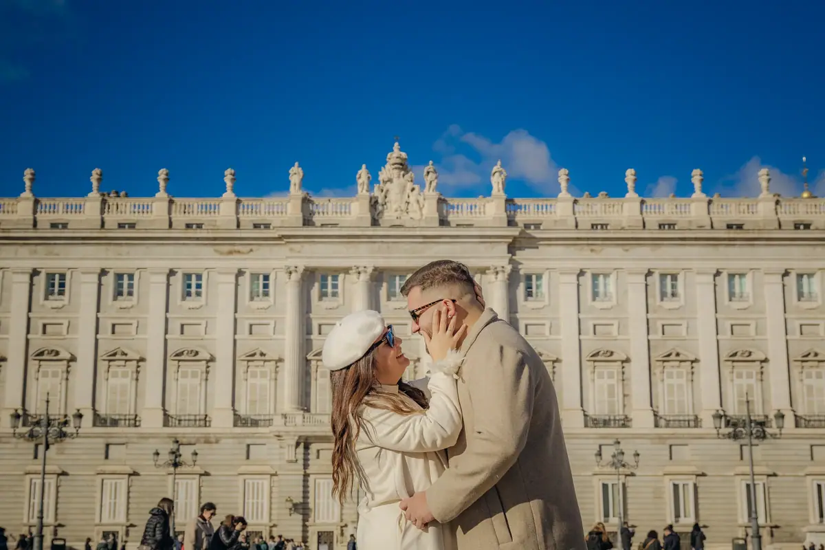 Couple embracing in front of a large stone palace under a blue sky